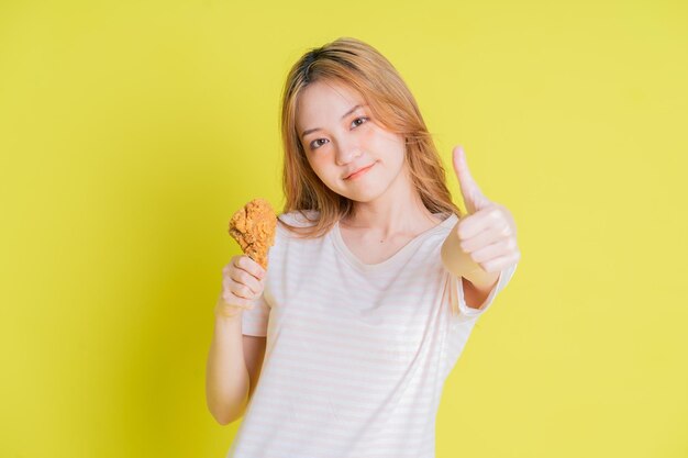 Imagem de uma jovem asiática comendo frango frito em fundo amarelo