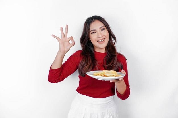 Foto imagem de uma jovem asiática sorridente segurando um prato de batatas fritas e gesticulando sinal de ok isolado no fundo branco