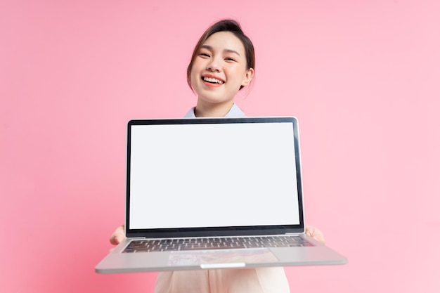 Imagem de uma jovem empresária asiática segurando laptop em fundo rosa