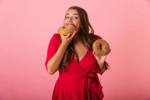 Imagem de uma jovem excitada isolada sobre uma parede rosa come donuts.