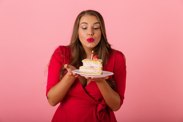 Imagem de uma jovem feliz isolada sobre a parede rosa segurando o bolo.
