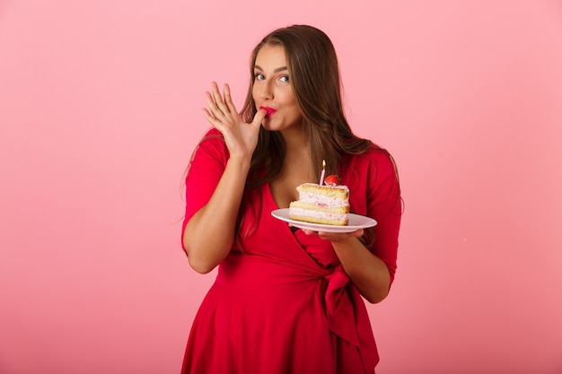 Imagem de uma jovem mulher com fome e animada isolada sobre o bolo segurando uma parede rosa.