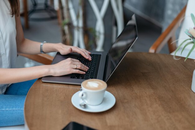 Imagem de uma jovem trabalhando em um laptop sentada em uma mesa de café