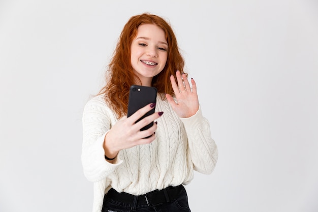 Imagem de uma linda jovem ruiva posando isolado sobre o fundo da parede branca tirar uma selfie.