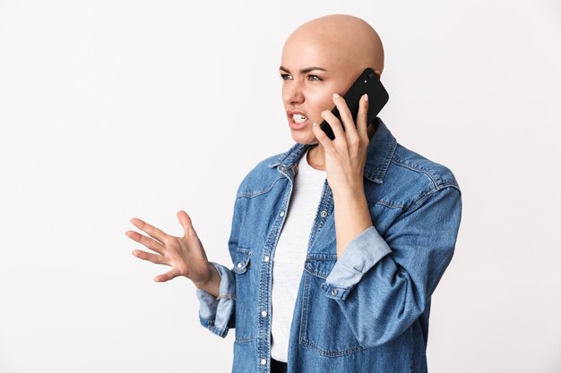 Imagem de uma linda mulher careca com raiva descontente posando isolado, falando por telefone celular.