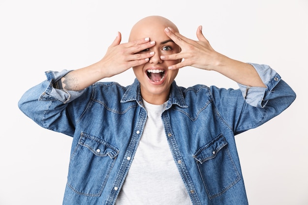 Foto imagem de uma linda mulher careca feliz posando isolada, cobrindo o rosto com as mãos.