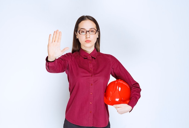 Imagem de uma linda mulher de óculos segurando o capacete e fazendo o sinal de pare.