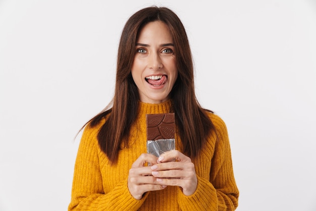 Imagem de uma linda mulher morena adulta sorrindo e segurando uma barra de chocolate isolada no branco