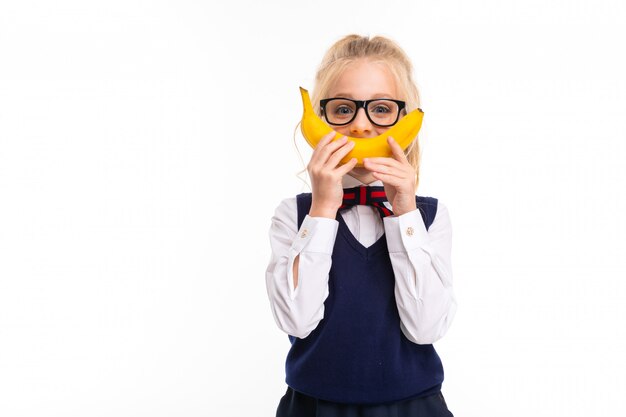 Imagem de uma menina de cabelo loiro segura uma banana e sorri com ela