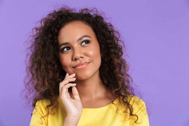 Imagem de uma mulher afro-americana morena com cabelo encaracolado, olhando para cima com um sorriso isolado na parede violeta