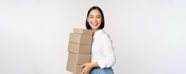 Imagem de uma mulher asiática feliz sorridente segurando uma pilha de caixas conceito de compras de entrega ou fundo branco de negócios