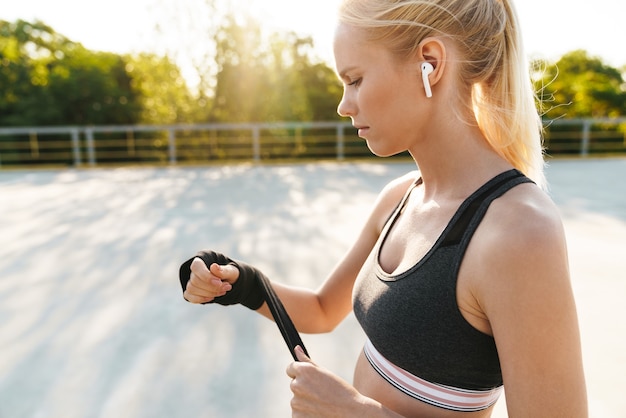 Imagem de uma mulher atraente em fitness treinando em roupas esportivas com envolvimento de mãos de boxe ao ar livre
