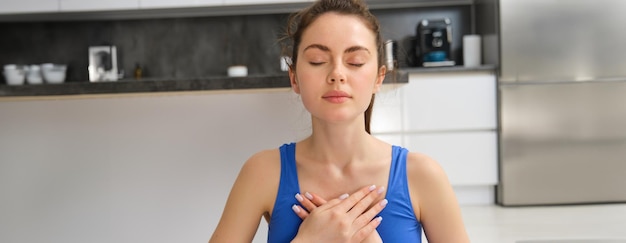 Foto imagem de uma mulher calma e relaxada meditando fazendo práticas respiratórias segurando as mãos no peito durante