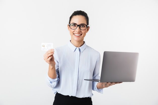 Imagem de uma mulher de negócios bonita isolada sobre uma parede branca, usando o computador portátil, segurando o cartão de crédito.