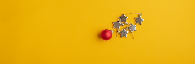 Imagem de visão ampla de bugiganga vermelha de Natal e estrelas douradas sobre fundo amarelo com muito espaço de cópia.