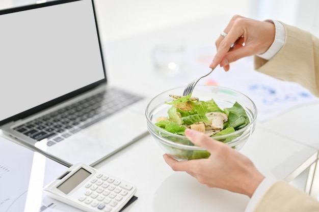 Imagem de visão lateral aproximada Uma empresária comendo uma tigela de salada saudável em sua mesa de escritório