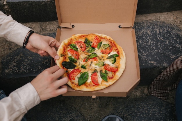 Imagem de vista superior de casal pegando fatias de pizza da caixa ao ar livre