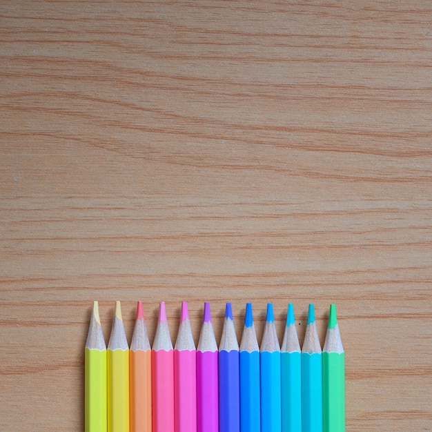 Imagem de vista superior de lápis apontados multicoloridos está colocando sobre uma mesa de madeira.