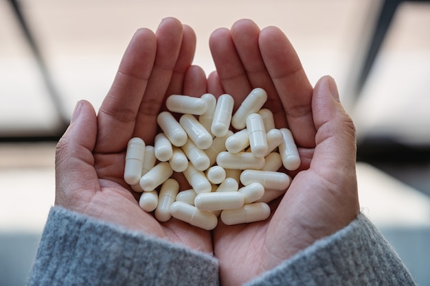 Imagem de vista superior de uma mulher segurando cápsulas de remédio branco