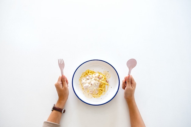 Imagem de vista superior de uma mulher segurando um garfo e uma colher, se preparando para comer espaguete carbonara na mesa