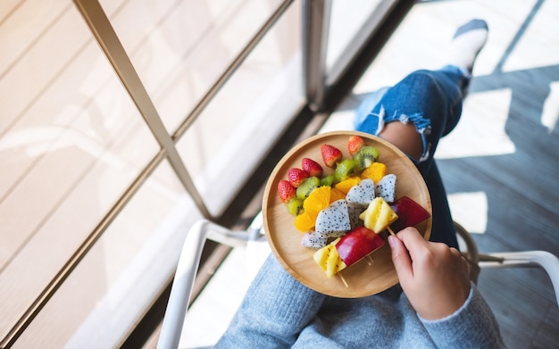 Imagem de vista superior de uma mulher segurando um prato de madeira com frutas frescas em espetos