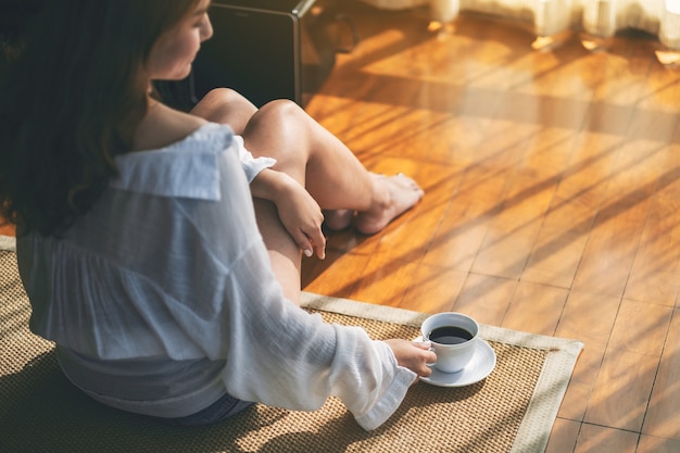 Imagem de vista superior de uma mulher sentada segurando uma xícara de café quente no chão pela manhã