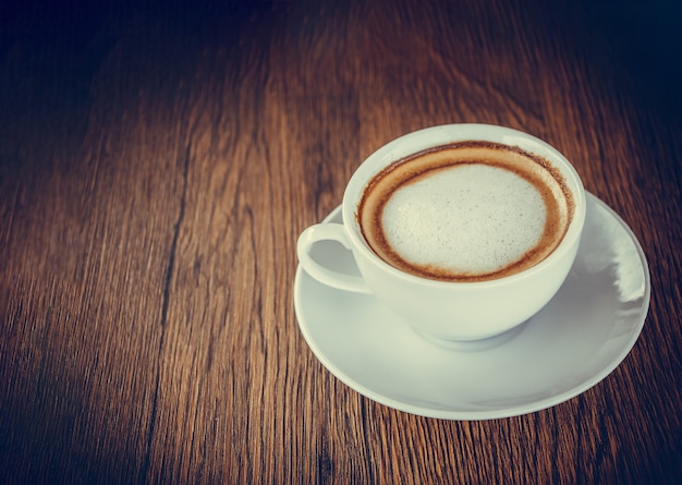 Foto imagem de xícara de café colocada sobre fundo de mesa de madeira com uso de espaço para exibição de textos