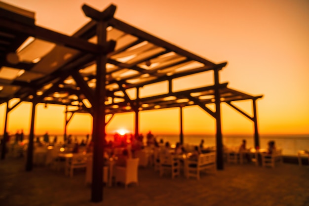 Imagem desfocada abstrata do terraço do restaurante ao ar livre na noite quente de verão, pôr do sol sobre o mar com