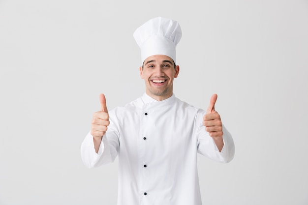 Imagem do chef de jovem animado bonito dentro de casa isolado sobre o fundo da parede branca, mostrando o gesto de polegares para cima.