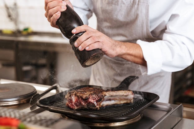 Foto imagem do chefe homem adulto em uniforme branco cozinhando a refeição com carne e vegetais na cozinha de um restaurante