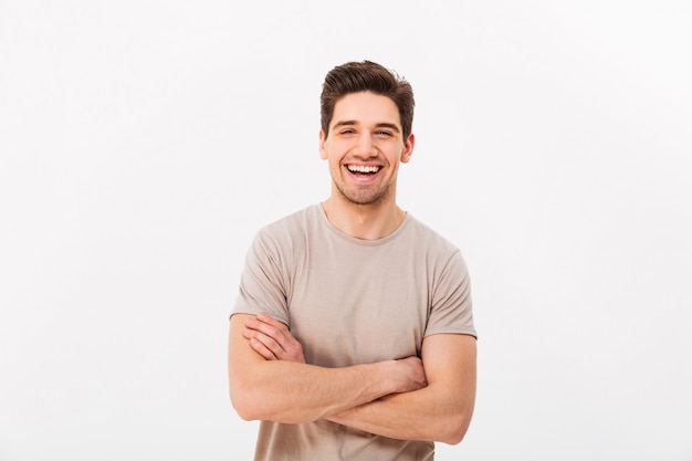 Imagem do homem sorridente feliz 30 anos com cerdas posando na câmera com as mãos cruzadas, isolado sobre a parede branca