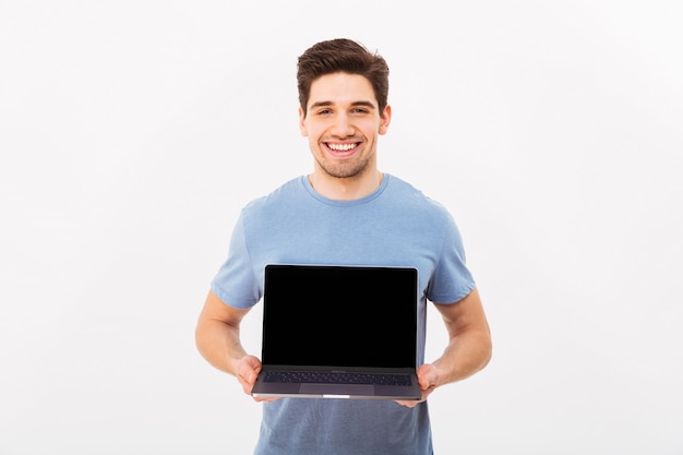 Imagem do homem sorridente feliz com cerdas segurando o caderno prateado demonstrando ou anunciando a tela do copyspace, isolada sobre a parede branca