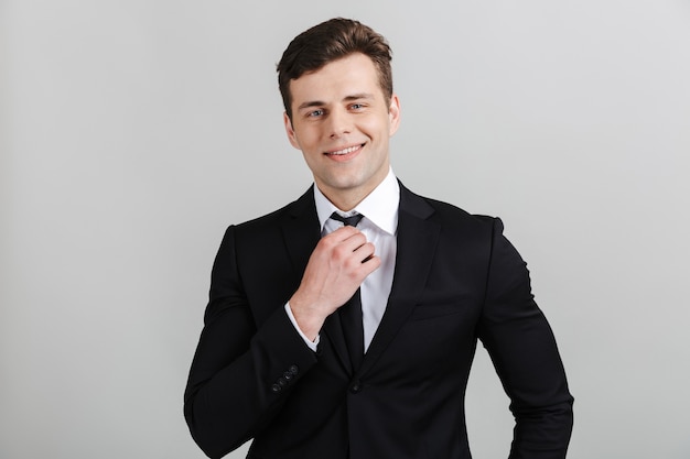 Foto imagem do jovem empresário confiante em um terno formal tocando a gravata e sorrindo