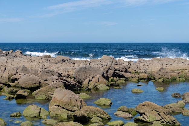 Foto imagem do respingo da onda do mar em rochas na costa em um dia ensolarado com céu azul