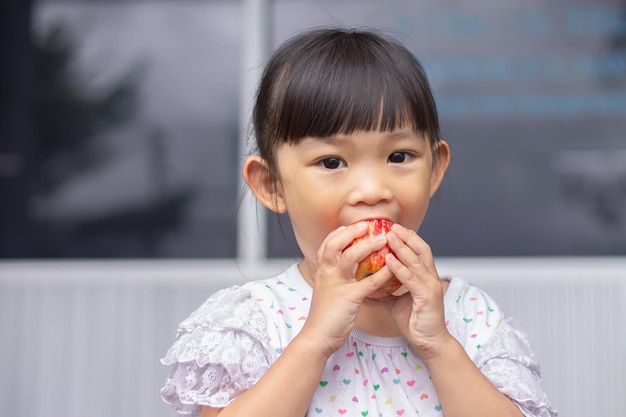 Imagem do retrato de 34 anos de idade do bebê Menina asiática feliz comendo e mordendo uma maçã vermelha Aproveite o momento de comer Comida saudável e conceito de criança Chupando os dedos na boca