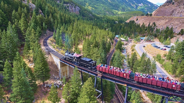 Imagem do velho trem para turistas atravessando ponte e riacho nas montanhas