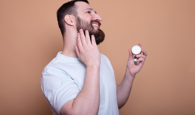 Imagem em close-up de um bonito homem barbudo segurando bálsamo para a barba