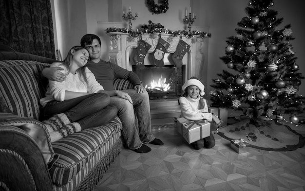 Imagem em preto e branco de uma jovem família feliz relaxando perto da lareira no Natal