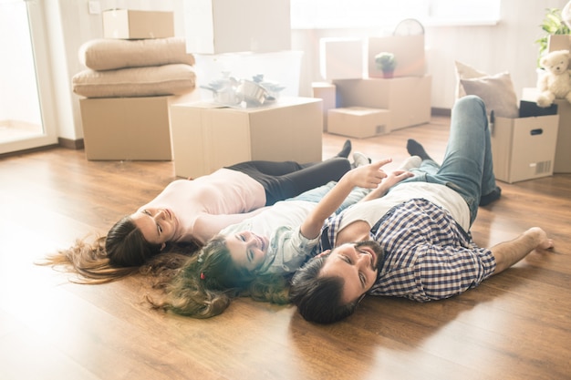 Imagem engraçada da família, deitado no chão em seu próprio apartamento novo. eles se divertem muito juntos. eles também estão procurando em algum lugar à direita.