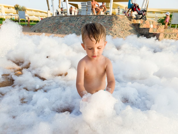 Imagem engraçada de um menino pequeno coberto de sabonete divertido na festa discoteca da praia do mar