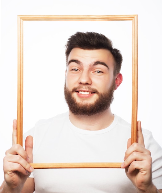 Imagem engraçada. jovem com barba segurando a moldura na frente de seu rosto e divertido hamming, isolado no branco.