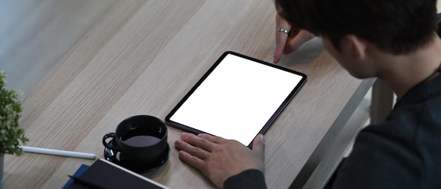 Imagem horizontal de jovem usando a caneta stylus, escrevendo no tablet digital enquanto está sentado na sala de estar.
