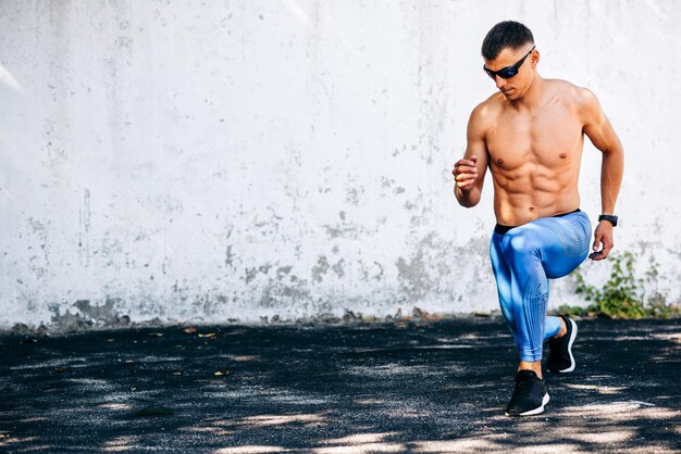 Imagem horizontal do jovem corredor apto homem alongamento antes de exercícios ao ar livre contra parede de concreto Atleta masculino se estende após treino fora Conceito de esporte e pessoas Copie o espaço para o seu texto