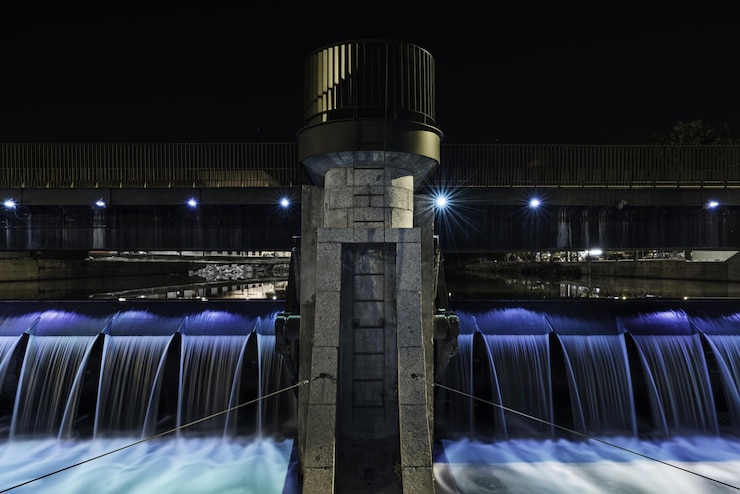 Foto imagem noturna de água caindo através de um pequeno reservatório do rio manzanares em madri com uma passarela de pedra com grades de metal