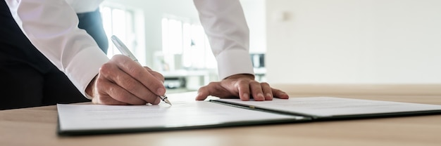 Imagem panorâmica do empresário assinando um documento ou contrato importante em pé em sua mesa de escritório.