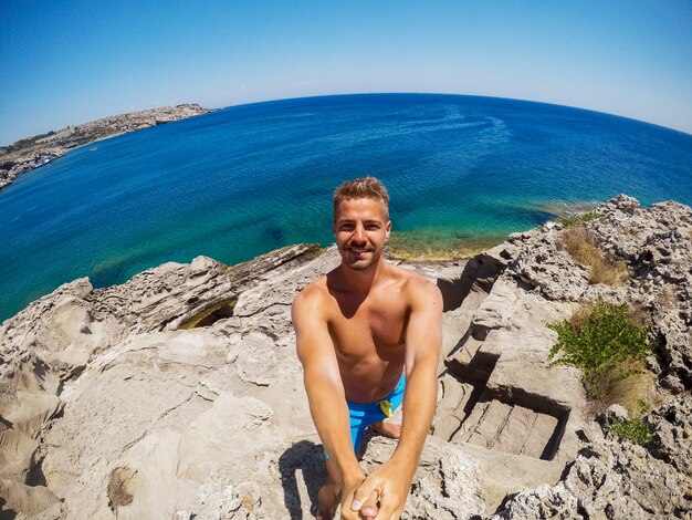 Imagem parcialmente borrada devido a gotas de água. Jovem explorador na aventura pronto para mergulhar. Selfie atirou em um dia de verão em uma rocha no meio do mar.