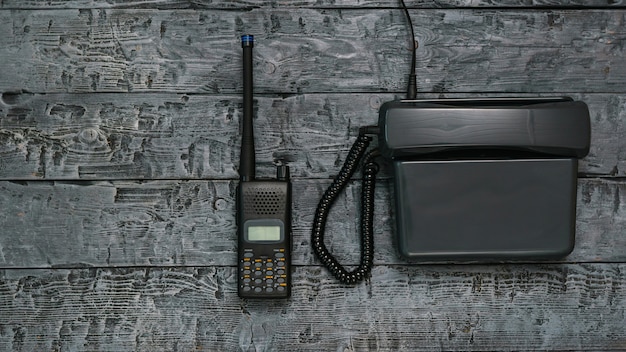 Imagem preto e branco de um walkie-talkie e telefone em uma mesa de madeira.