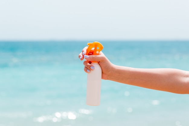 Imagem recortada da mão de uma mulher segurando o protetor solar spray na praia.