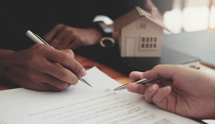 Imagem recortada de agente imobiliário auxiliando o cliente a assinar o papel do contrato na mesa com a maquete da casa