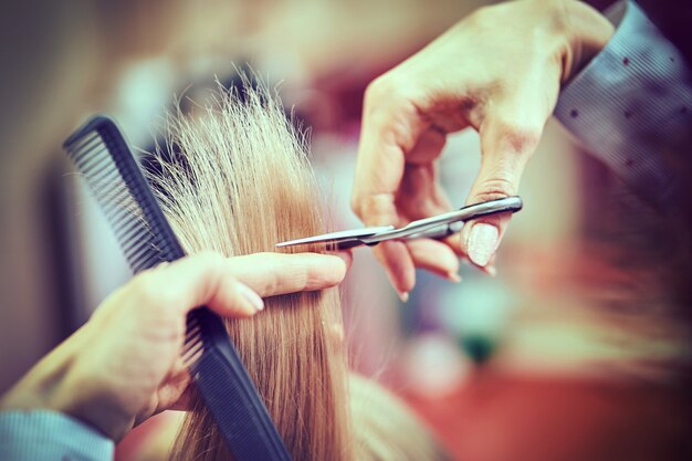 Imagem recortada de cabeleireiro aparando pontas de cabelo loiro